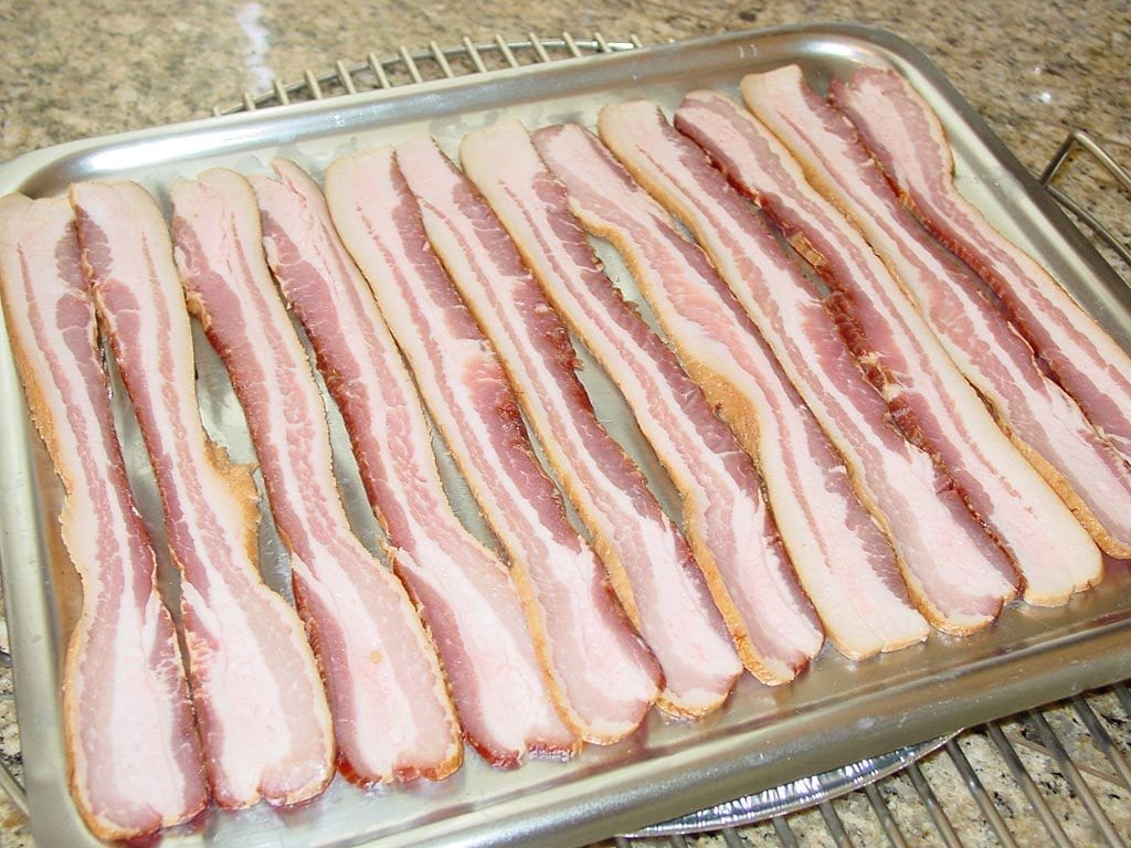 Raw strips of bacon arranged on a broiler pan