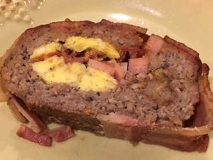 A slice of breakfast bacon weave fatty with tater tot filling on a plate