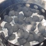 Additional unlit briquettes spread over hot charcoal