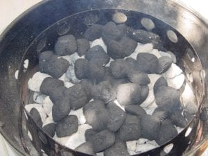 Additional unlit briquettes spread over hot charcoal