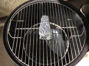 Foil-wrapped smoke wood chunk on top cooking grate