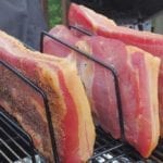 Three pieces of cured pork belly smoking in the Weber Bullet