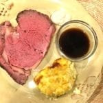 Prime rib on a plate with au jus and corn casserole
