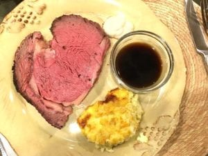 Prime rib on a plate with au jus and corn casserole