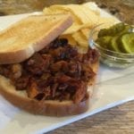 Rib sandwich served with potato chips and pickles