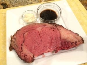 Slice of rib roast on plate with au jus and creamy horseradish
