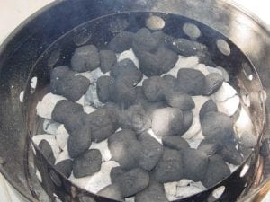 Additional unlit briquettes spread over hot charcoal