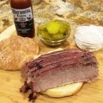 Brisket sandwich with pickles, onions, and sauce on the side