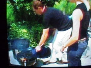 From the television show Boy Meets Grill on the Food Network. The episode was called "Boy Meets Texas Girl" and aired in 2004. Bobby Flay makes brisket with his girlfriend Stephanie March and places the water pan directly on top of the charcoal chamber full of hot coals and wood chips. A classic WSM moment! By Tom Chilton, captured on TIVO