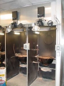 Test stations in the Weber burn room. A charcoal ring hangs on the back wall. The circular thermocouple array is shown about 12" above and to the left of the kettle on the right. The gray box outside each station is a timer. The black box above each station is an interface that connects test equipment to a monitoring computer.