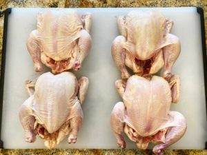 Four unwrapped, patted dry Cornish game hens on cutting board