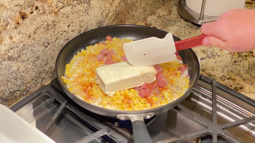 Adding corn, ham, milk, cream cheese, and spices