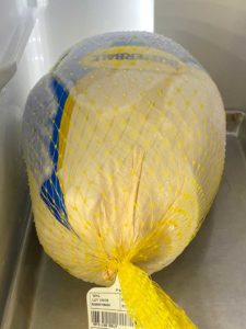 Frozen turkey thawing in the refrigerator over rimmed baking sheet pan