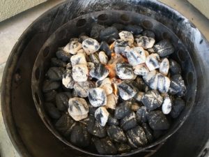 Lit charcoal poured over unlit briquets and wood chunks